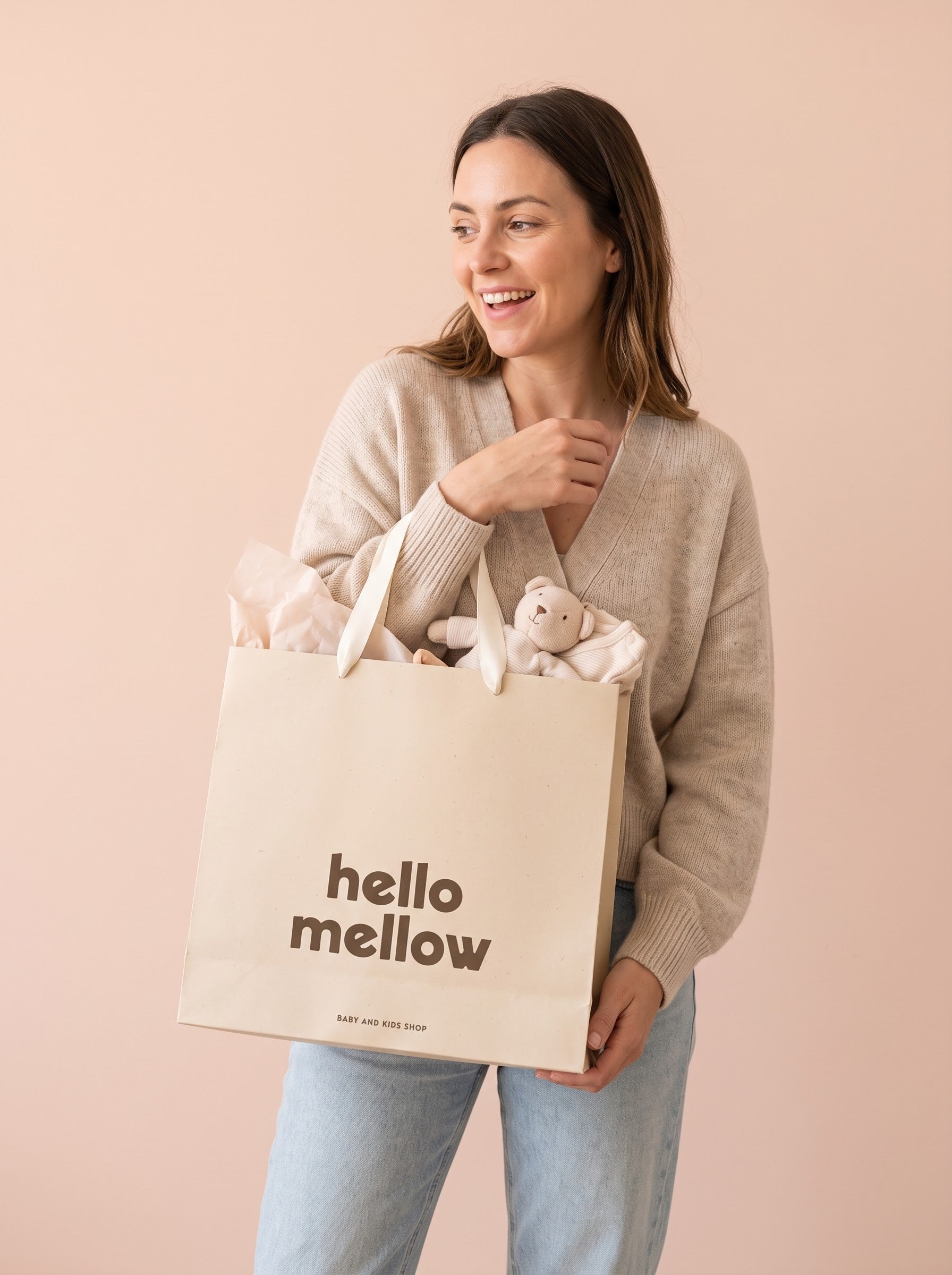 Mujer sonriendo con la bolsa de regalo Hello Mellow llena de regalos para bebé