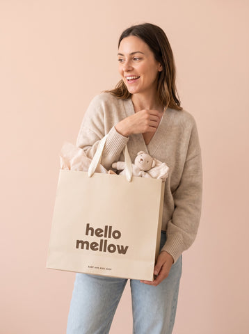 Mujer sonriendo con la bolsa de regalo Hello Mellow llena de regalos para bebé